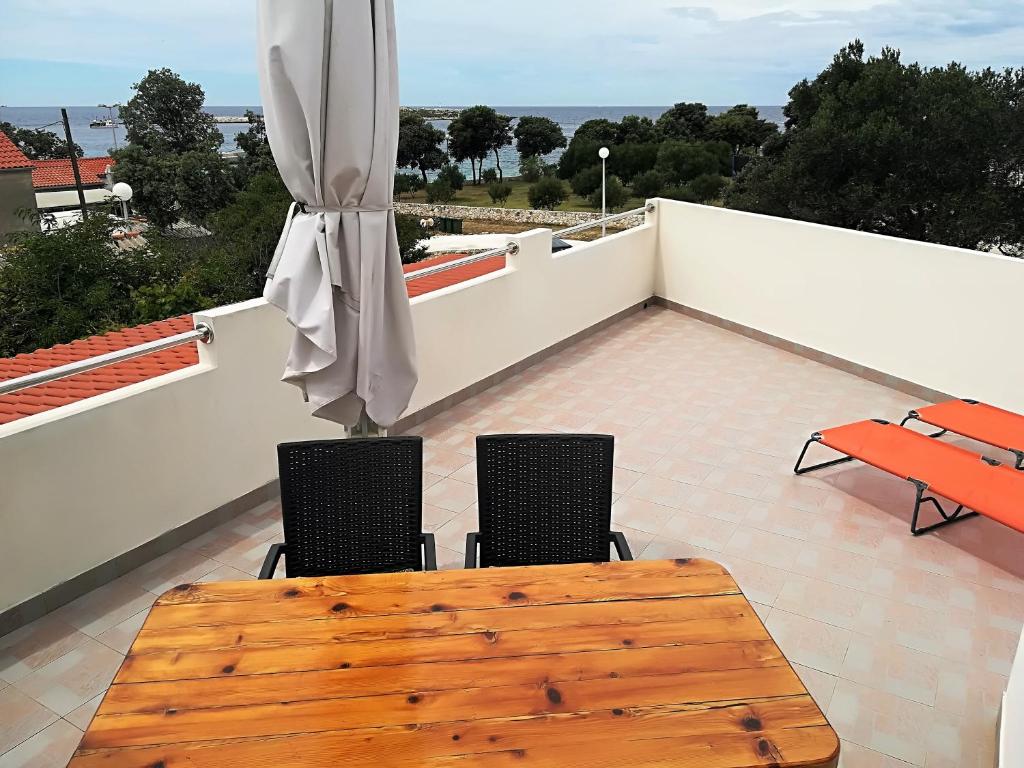 einen Holztisch und Stühle auf einem Balkon mit Sonnenschirm in der Unterkunft Apartman Rosanda in Premuda