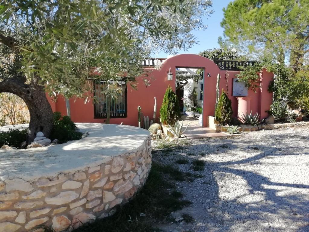 a red house with a stone wall and a tree at Casa Rural Delta del Ebro Ecoturismo in Camarles