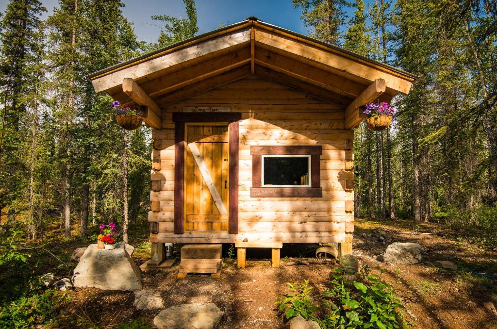 una pequeña cabaña de madera en el bosque con flores en Blackburn Cabins - McCarthy, Alaska en McCarthy