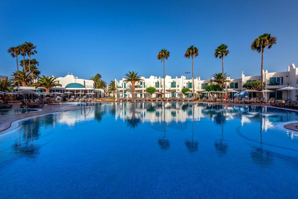 uma grande piscina com palmeiras e edifícios em Barceló Corralejo Sands em Corralejo