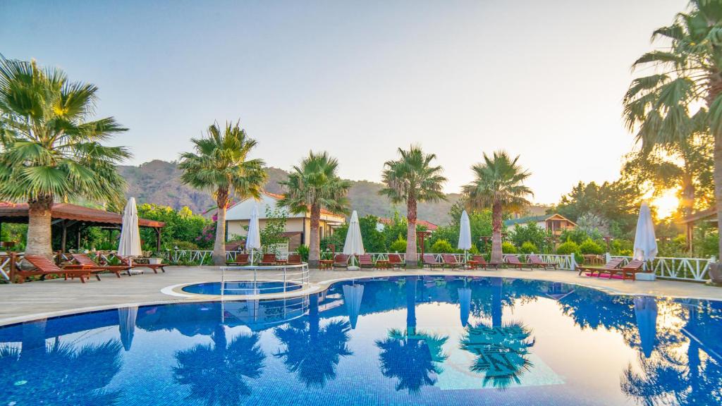 a large swimming pool with palm trees and chairs at Nerissa Hotel in Cıralı