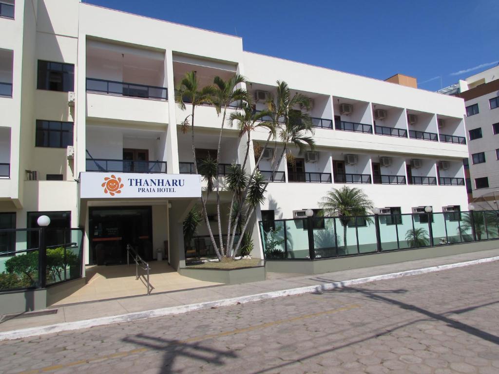 a large white building with palm trees in front of it at Thanharu Praia Hotel in Anchieta