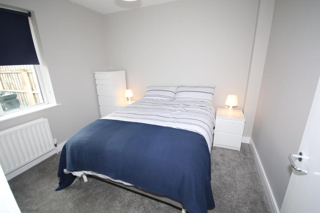 a bed in a white room with a blue blanket at Strand House 2 in Portstewart