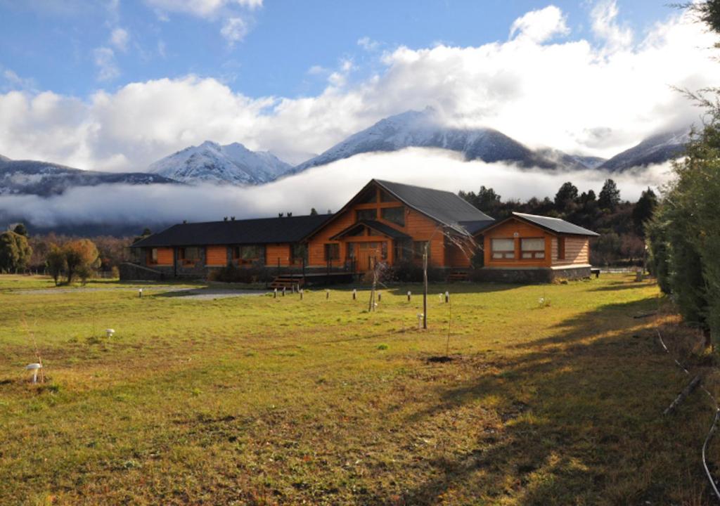 una casa en un campo con montañas en el fondo en Hosteria Ruca Kitai en Villa Lago Rivadavia