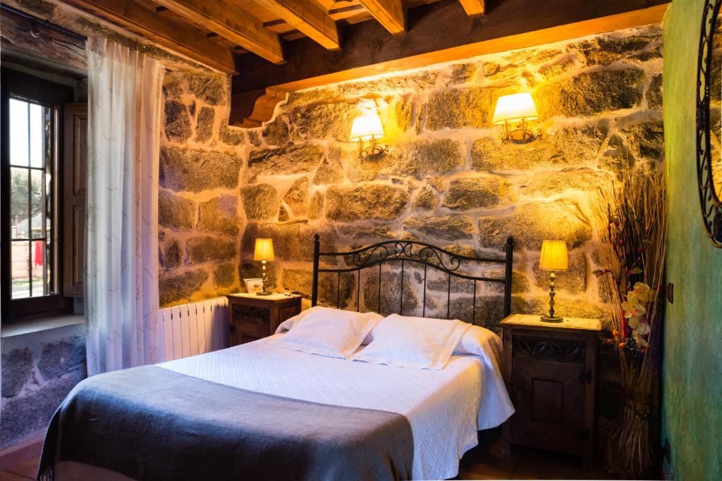 a bedroom with a stone wall with a bed and two lamps at El Mirador del Alberche 1 in Navaluenga
