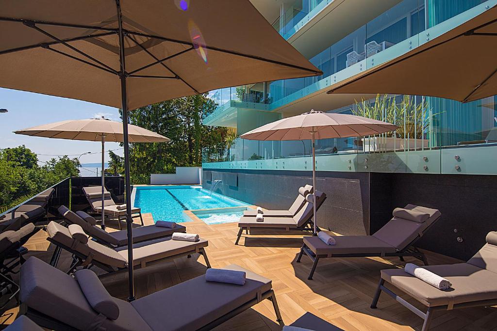 奧帕蒂亞的住宿－Deluxe Apartments Opatija，一座带椅子和遮阳伞的游泳池位于一座建筑旁边
