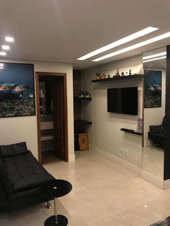 ein Wohnzimmer mit einem schwarzen Sofa und einem Flachbild-TV in der Unterkunft Praia do Forte Apt. in Praia do Forte