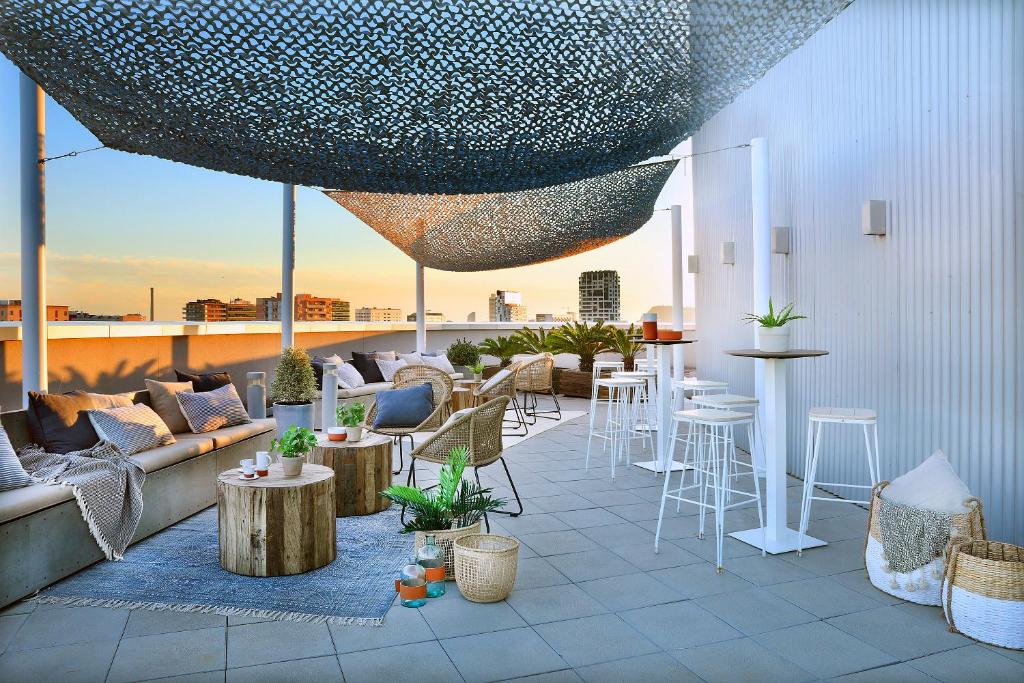 een dakterras met een bank, tafels en stoelen bij Hotel Barcelona Condal Mar Affiliated by Meliá in Barcelona