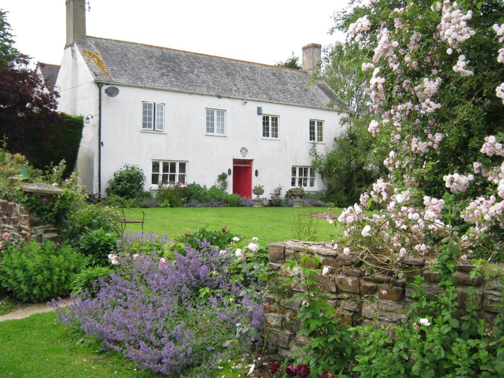 a white house with a red door and some flowers at Hollamoor Farm in Barnstaple