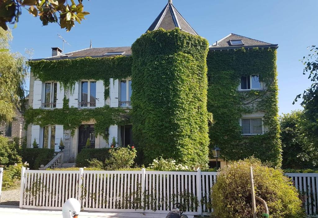 uma grande casa coberta de hera com uma cerca branca em Chambres d'hôtes Les Magnolias em Saint-Chéron