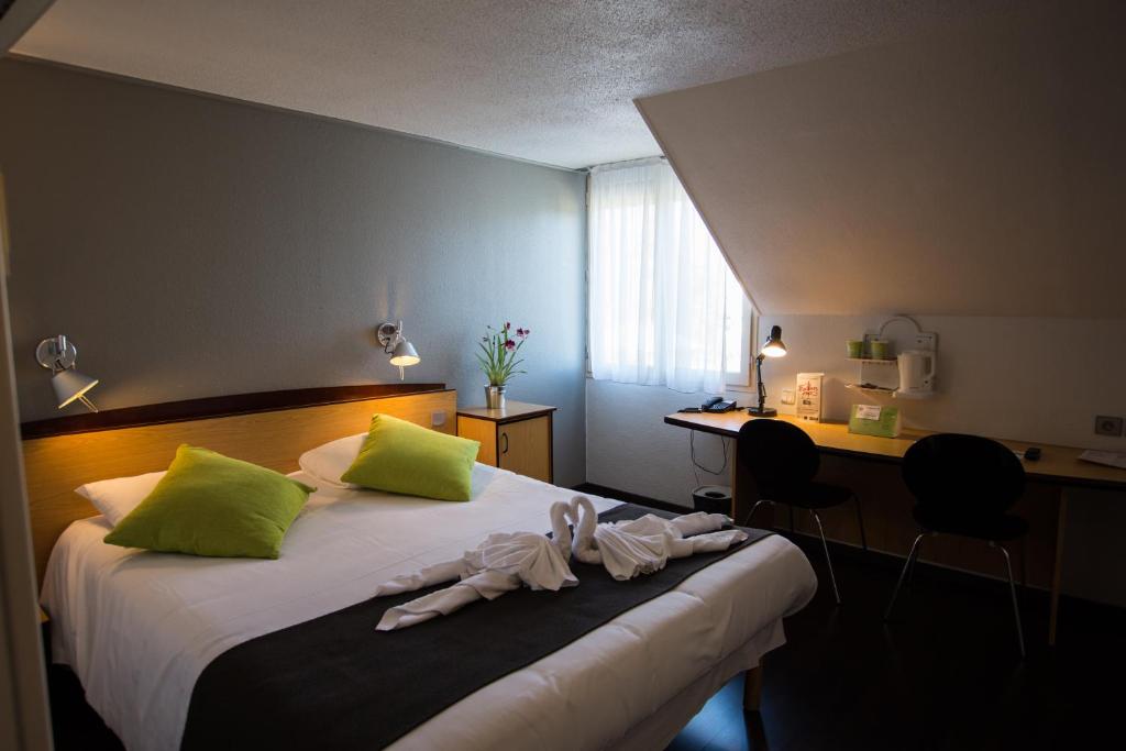 a bedroom with a bed with green pillows and a desk at Campanile Saumur in Saumur