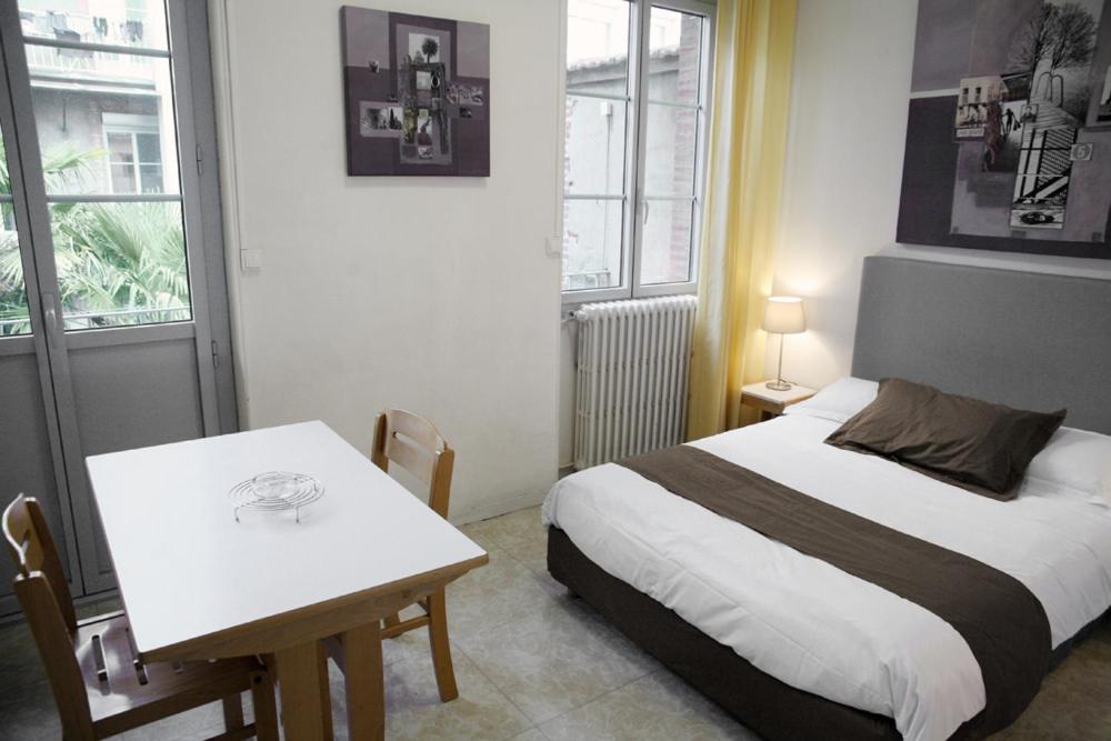 a bedroom with a bed and a table and windows at Résidences Guerlin in Toulouse