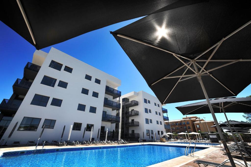 a pool with chairs and umbrellas next to a building at Leo Deluxe Punta Umbría in Punta Umbría