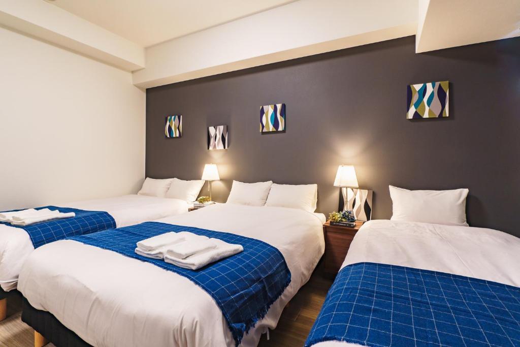 Habitación con 3 camas con sábanas azules y blancas. en IKIDANE Residential Hotel SHIMANOUCHI, en Osaka