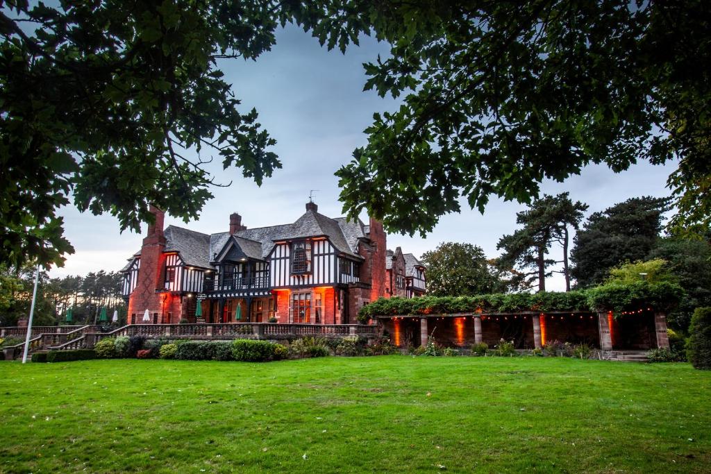 une maison ancienne avec une pelouse verte devant elle dans l'établissement Inglewood Manor, à Ledsham