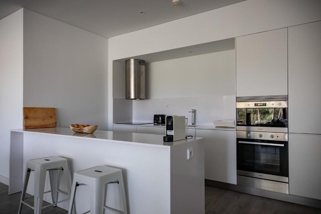 a white kitchen with a counter and stools in it at Pestana Troia Eco-Resort & Residences in Troia