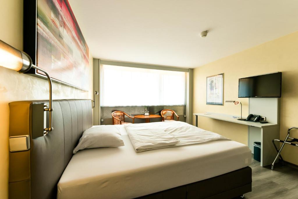 a bedroom with a bed with a desk and a window at City Hotel Heilbronn in Heilbronn