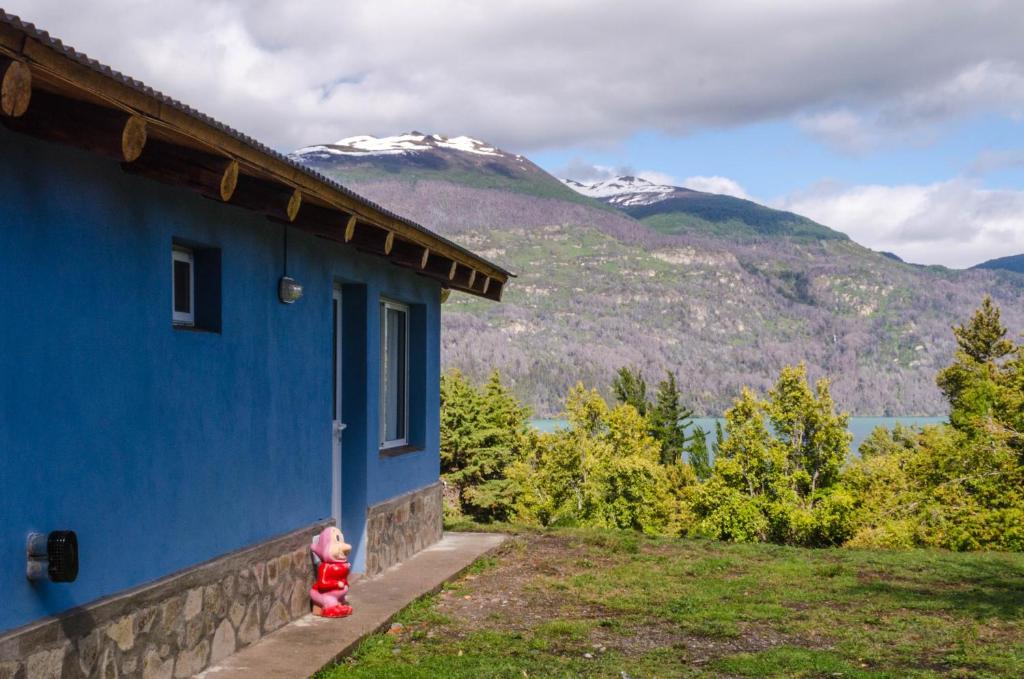 a child standing next to a blue building with mountains in the background at Rincón del Sol in Parque Nacional Los Alerces