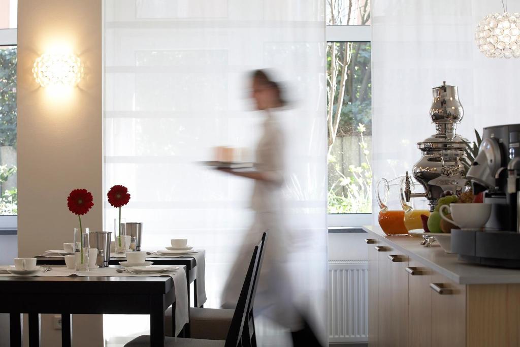 a woman is walking through a kitchen with a table at Hotel Maximilians in Essen