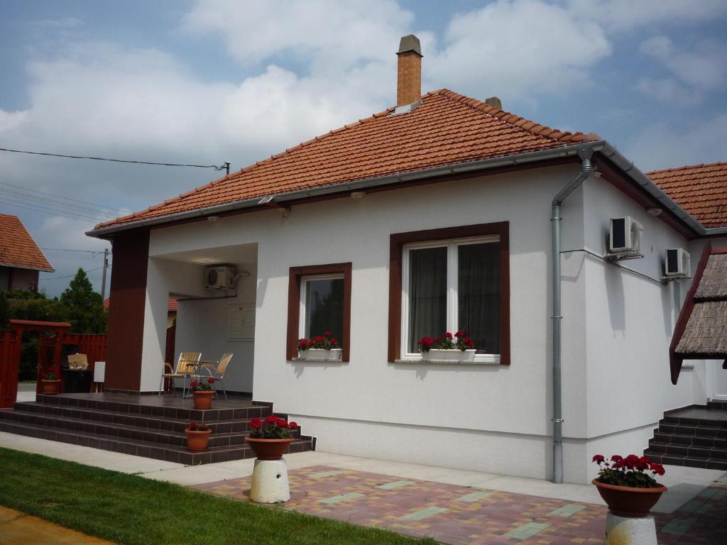 a small white house with two windows and flowers at Mórafészek vendégház in Mórahalom