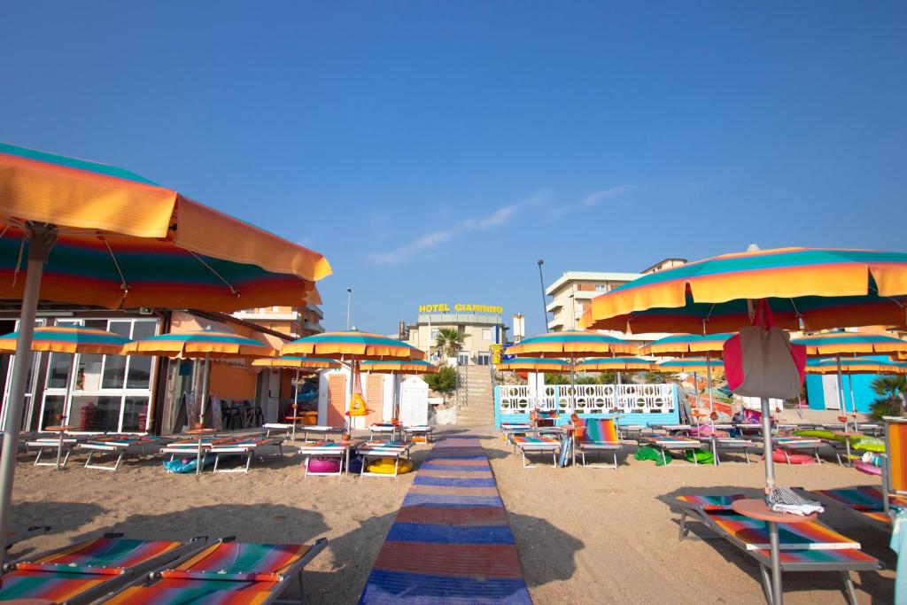 una spiaggia con sedie, ombrelloni, tavoli e sedie di Hotel Giannino a Porto Recanati