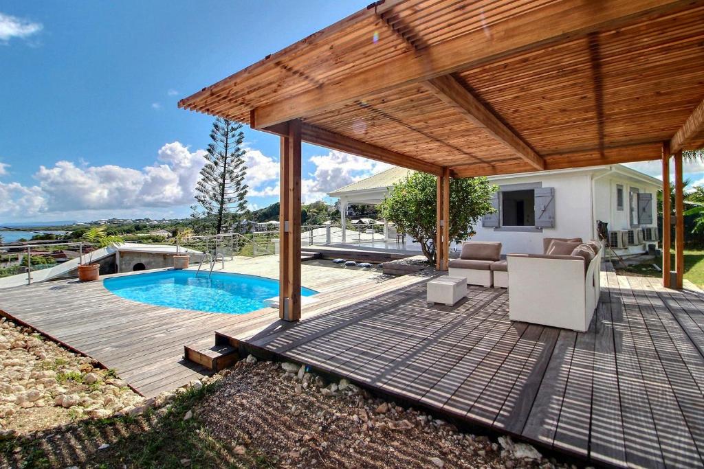 una terraza de madera con piscina y pérgola de madera en Villa Thomana, piscine, vue mer et plage à 100 m !, en Le Moule