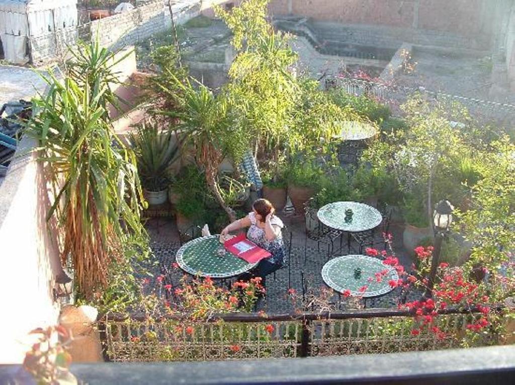 una mujer sentada en una mesa en un jardín en Riad Hôtel Belleville Marrakech, en Marrakech