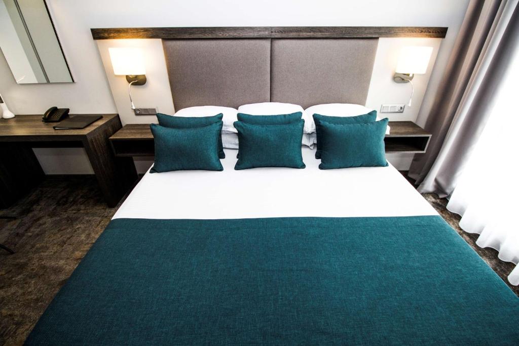 a bedroom with a large bed with blue pillows at Best Western PLUS Premium Inn in Sunny Beach