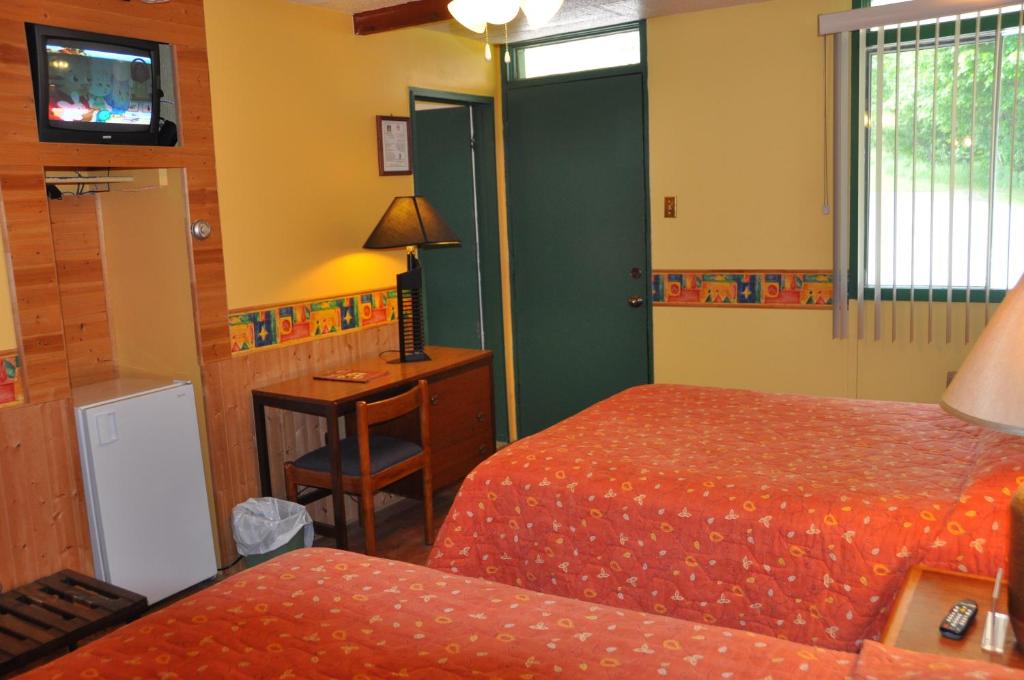 a room with two beds and a desk and a television at Le Boisé du Lac in Mont-Tremblant