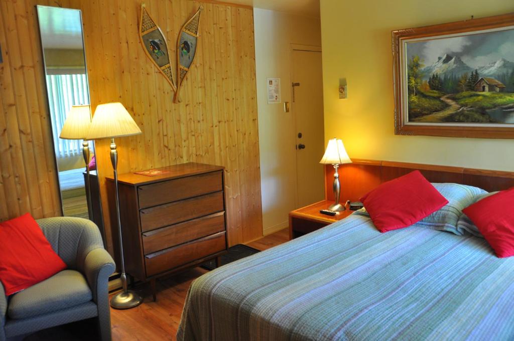 a bedroom with a bed with red pillows and a chair at Le Boisé du Lac in Mont-Tremblant