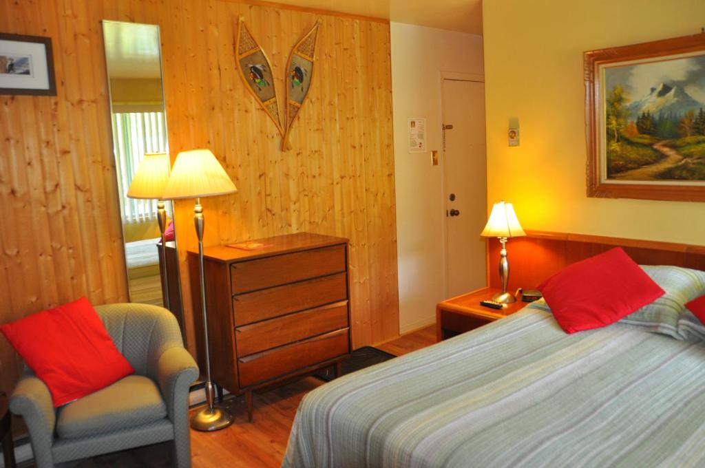 a bedroom with a bed and a chair and two lamps at Le Boisé du Lac in Mont-Tremblant