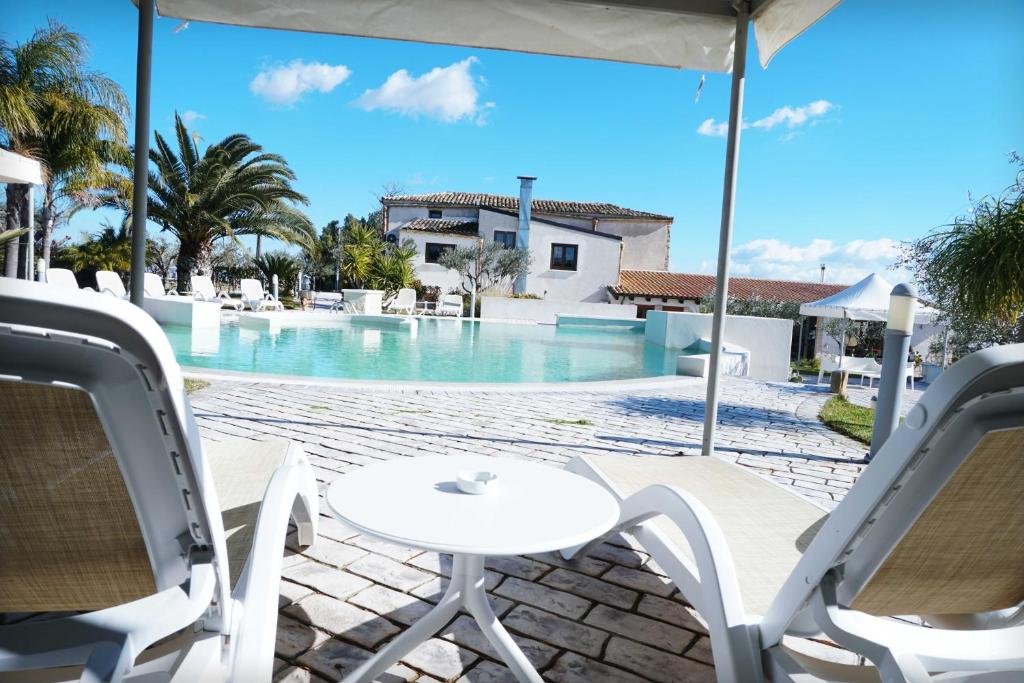 un patio con tavolo e sedie di fronte alla piscina di Agriturismo Baglio San Nicola a Naro