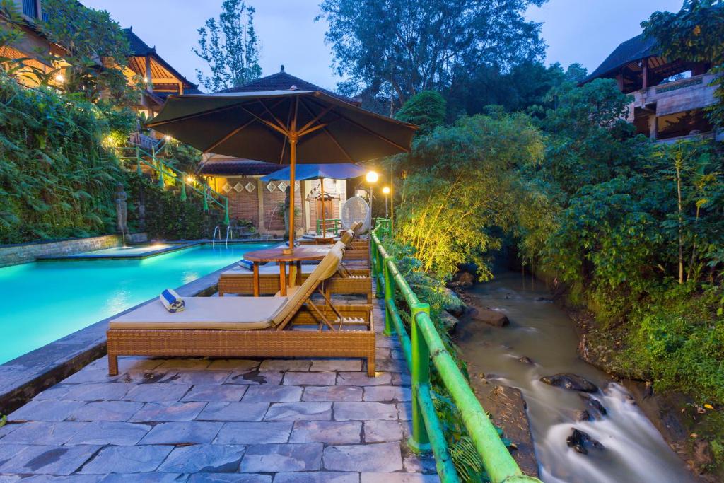 a pool with tables and an umbrella next to a river at Ani's Villas in Ubud