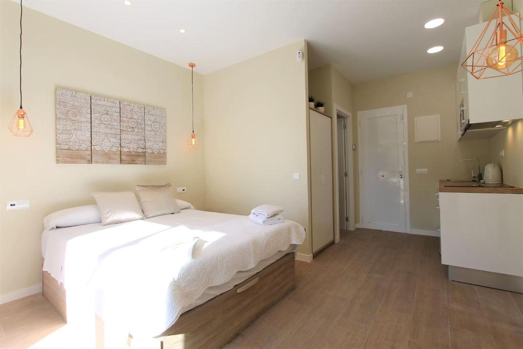 a bedroom with a large white bed and a kitchen at Petit Bijou - Beach apartment III in Castelldefels