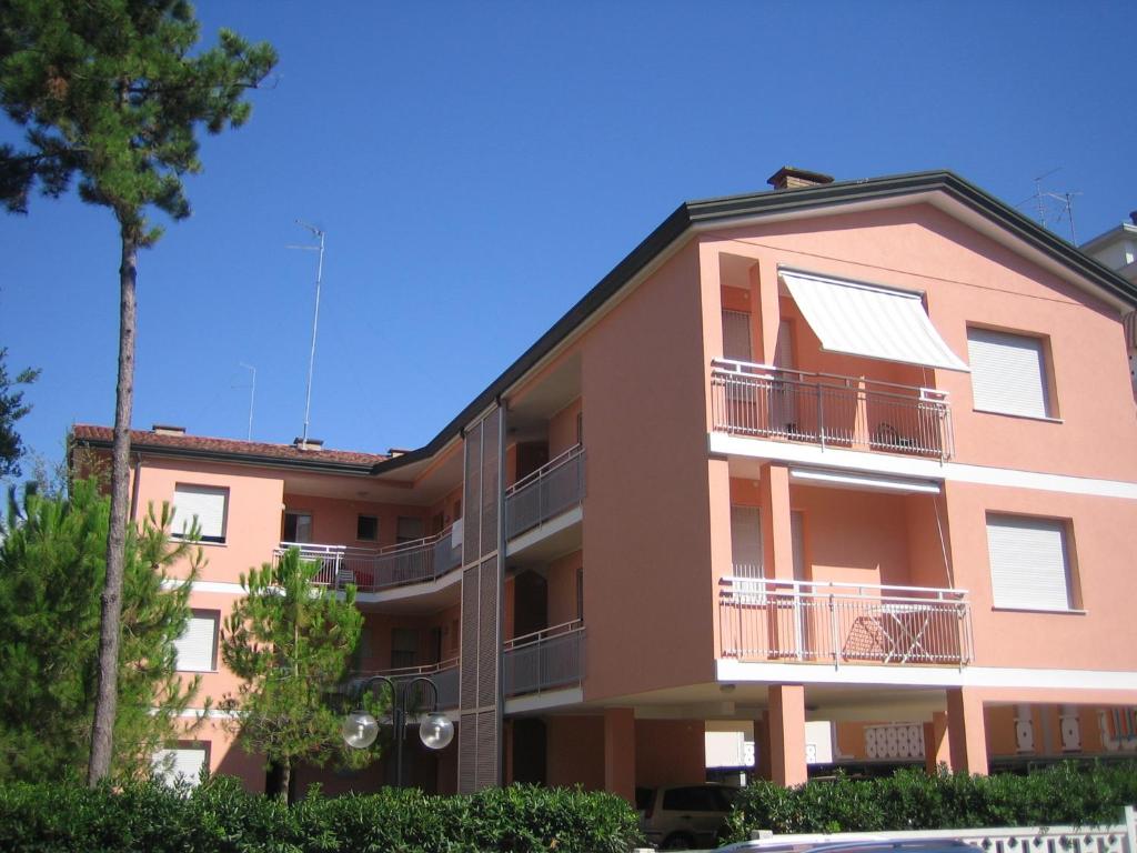 un edificio de apartamentos rosa con un árbol delante de él en Appartamenti Dei Pini, en Bibione