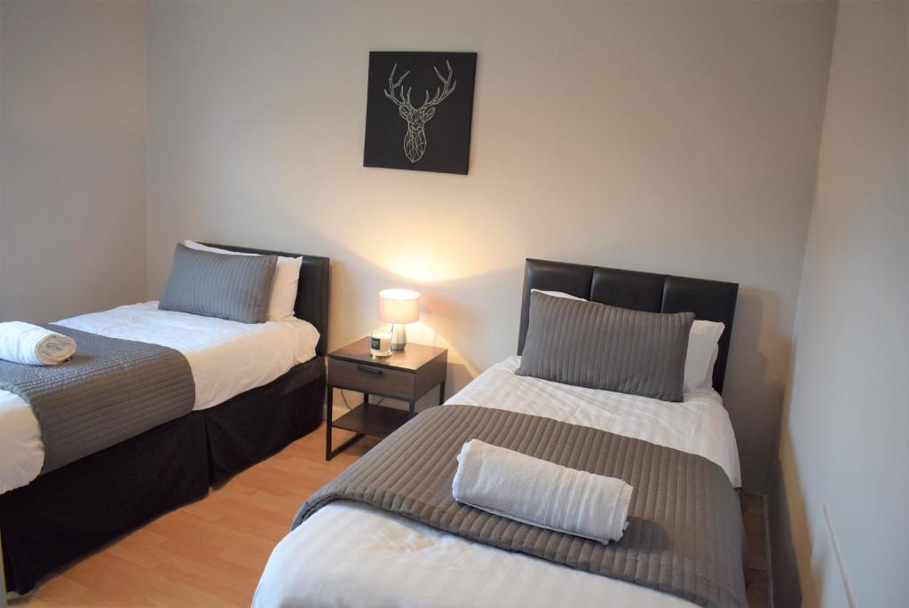 a bedroom with two beds and a night stand with a lamp at 3 Bedroom-Kelpies Serviced Apartments Bruce in Falkirk