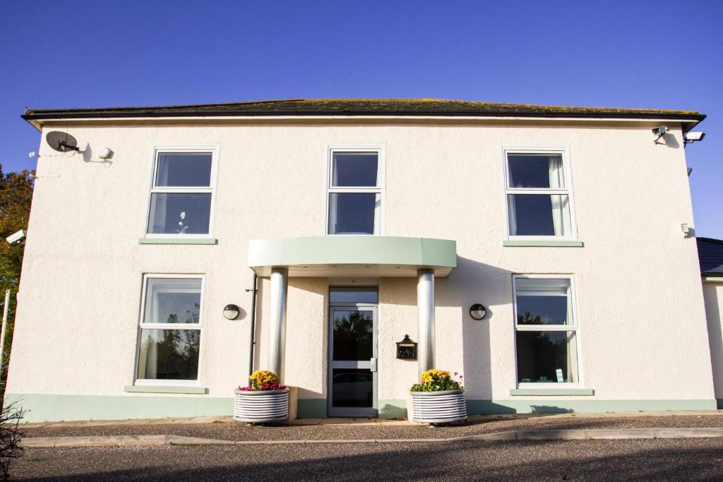 Fair Oak House Exeter Airport في إكسيتير: بيت ابيض وامامه قدور ورد