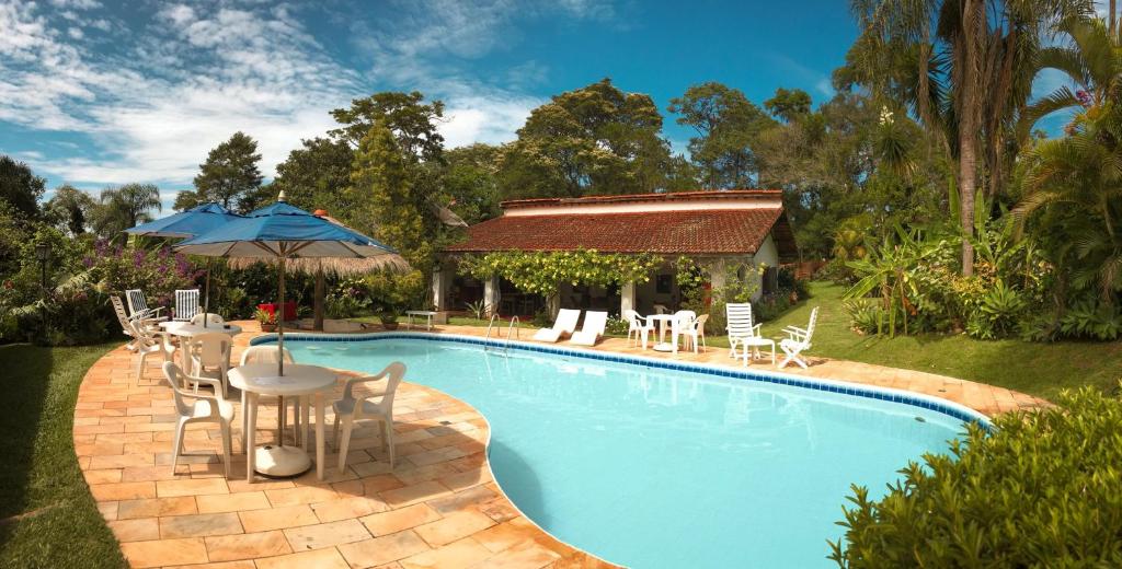 une piscine avec une table et des chaises ainsi qu'une maison dans l'établissement Pousada da Gibinha, à Campina do Monte Alegre