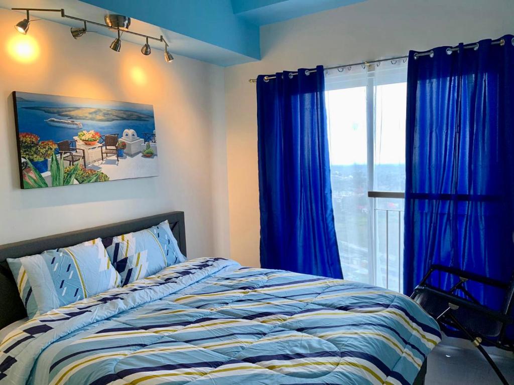 Tagaytay Condotel with PS4 near skyranch في تاجيتاي: غرفة نوم بسرير والستائر الزرقاء ونافذة