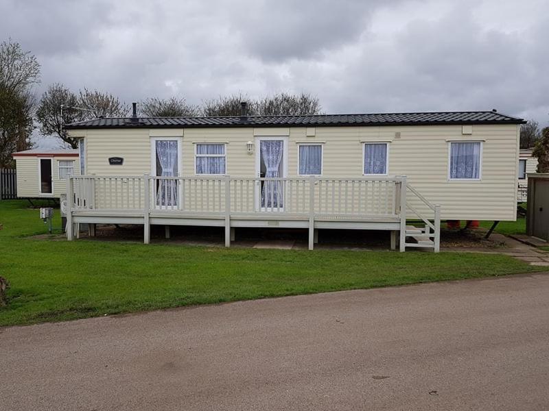 a white house with blue windows and a porch at S460 8 BERTH CARAVAN ON THE GOLDEN PALM CHAPEL ST LEONARDS in Chapel Saint Leonards