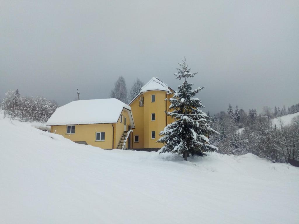 uma casa amarela na neve com uma árvore de Natal em Guest House Magnat em Verkhne-Studënyy