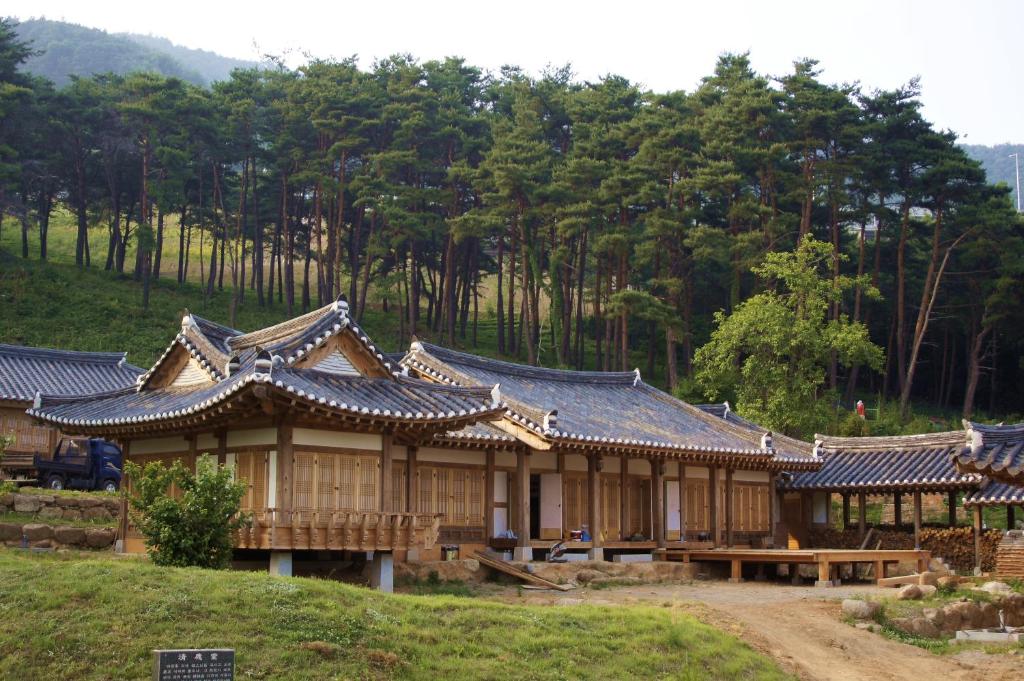 un grupo de edificios de madera con un bosque en el fondo en Korean Traditional House - Chungnokdang, en Boseong