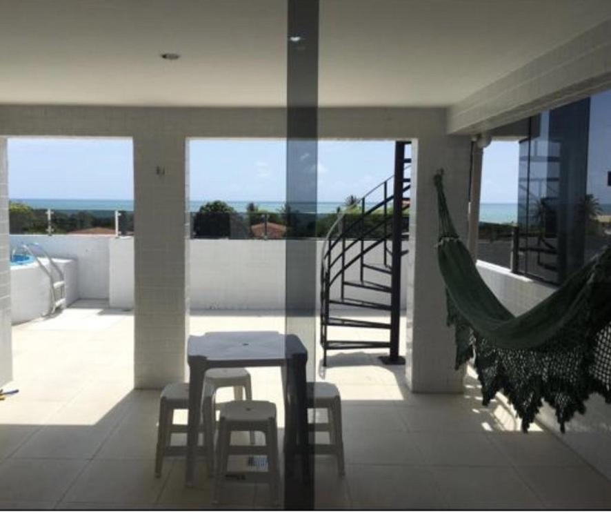 a balcony with a table and chairs and a hammock at Cobertura Vista Ampla para o Mar in Jacumã