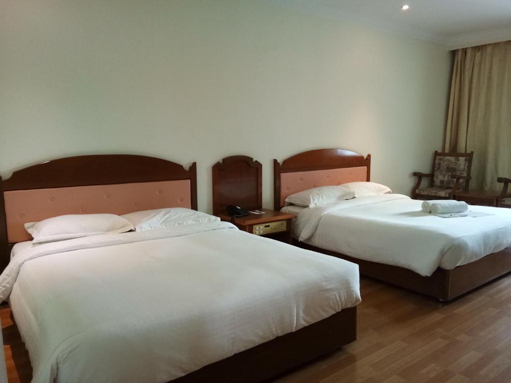 Purnama Hotel في ليمبانغ: سريرين في غرفة الفندق ذات شراشف بيضاء