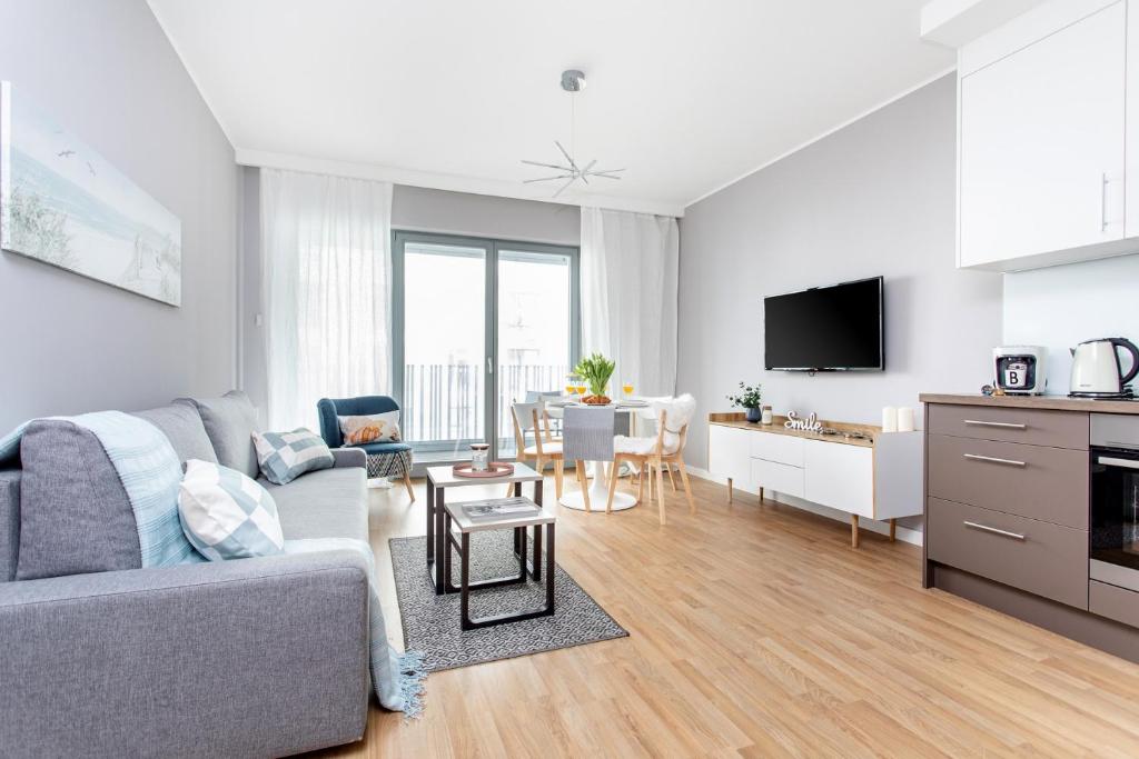 a living room with a gray couch and a kitchen at Seaside Beach 150m do Plaży - Praia Apartments - Polsat Plus Arena in Gdańsk