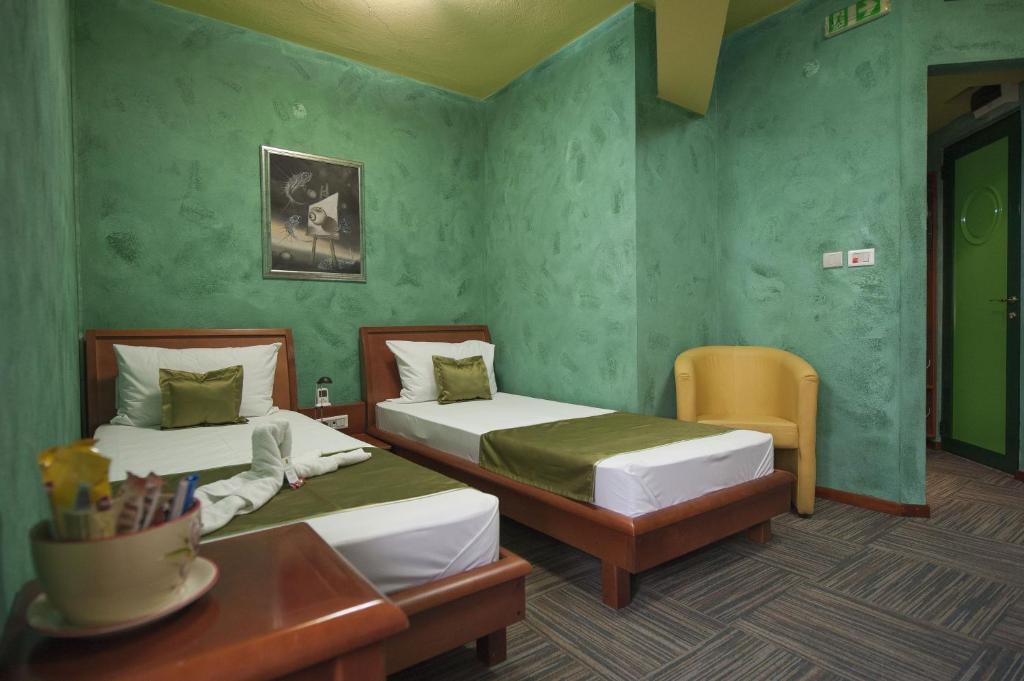 two beds in a room with green walls and a table at Hotel Kerber in Podgorica