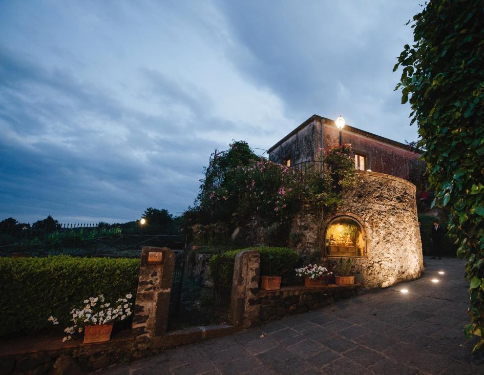 a building with a stone wall and flowers in a courtyard at Case Perrotta in SantʼAlfio