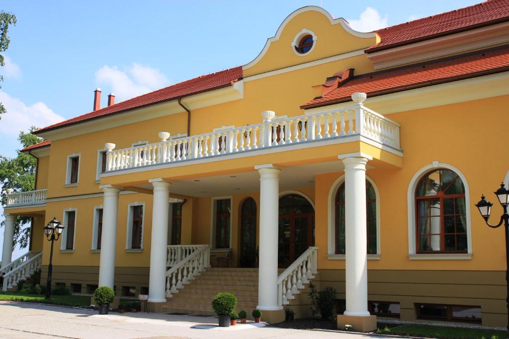 a yellow house with a balcony and stairs at Hotel *** Plauter Kúria in Veľký Meder