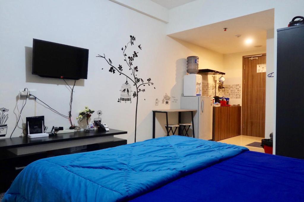 a bedroom with a blue bed and a desk and a tv at Bacup Studio Apartment @Galeri Ciumbuleuit in Bandung