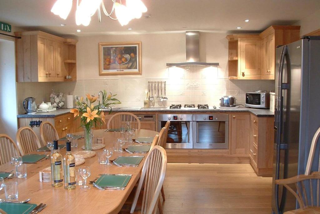 a kitchen with a long table with chairs and a refrigerator at Arbor Holiday Cottages in Southam